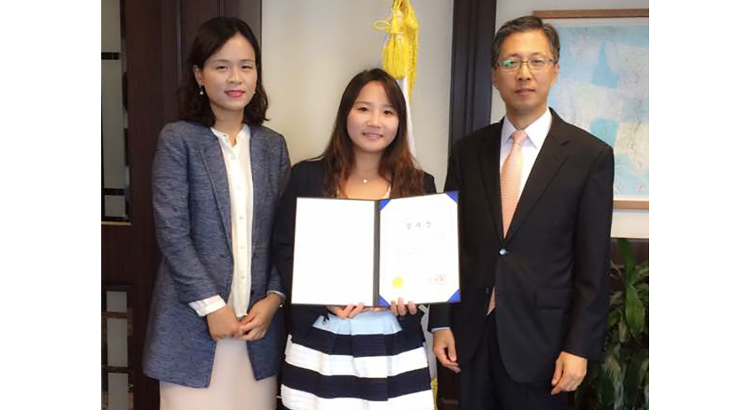 Hanae Kim holds her award while surrounded by representatives of the Ministry of Education